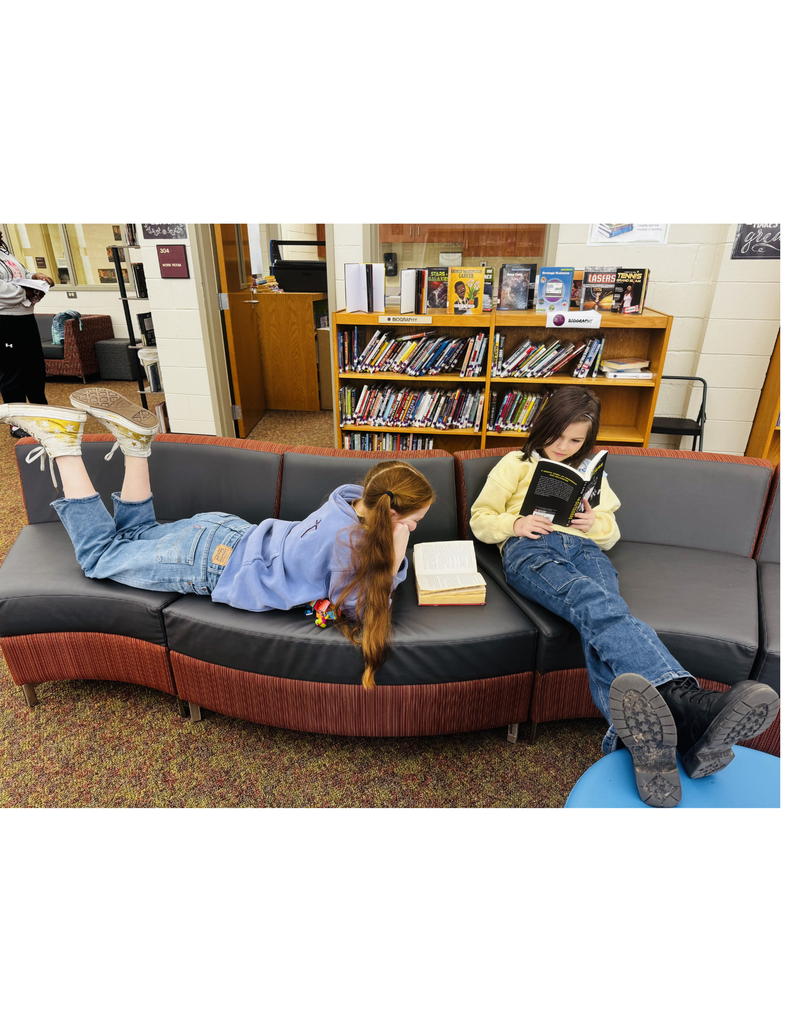 2 Students lying  on a couch reading.