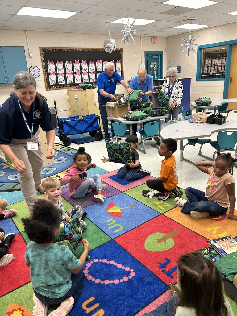 Students sitting on the carpet as they are handed dinosaur print pillows.