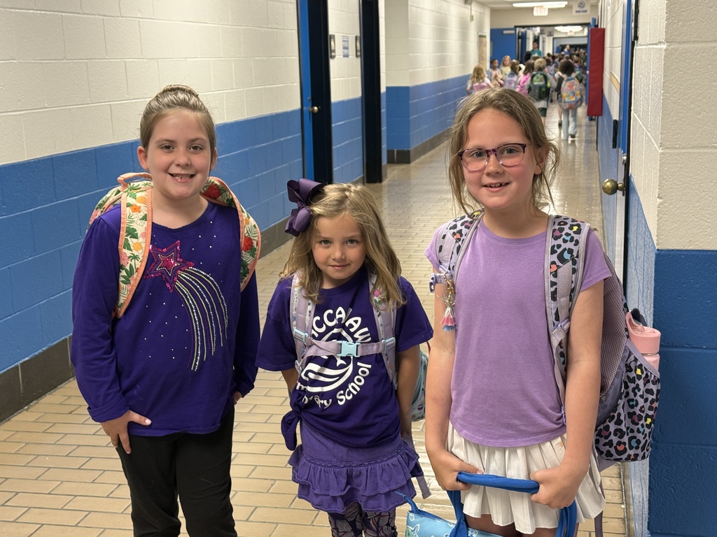Three students in a school hallway wearing purple and carrying backpacks.