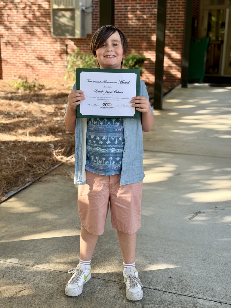 Student holding an achievement award outside of a school building.