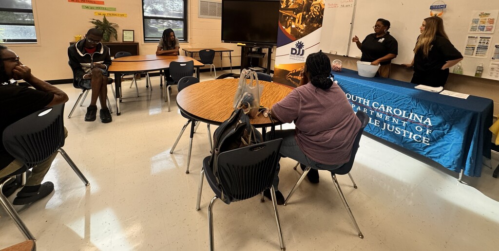 Students seated around tables in a classroom engaging in the SC Department of Juvenile Justice presentation.