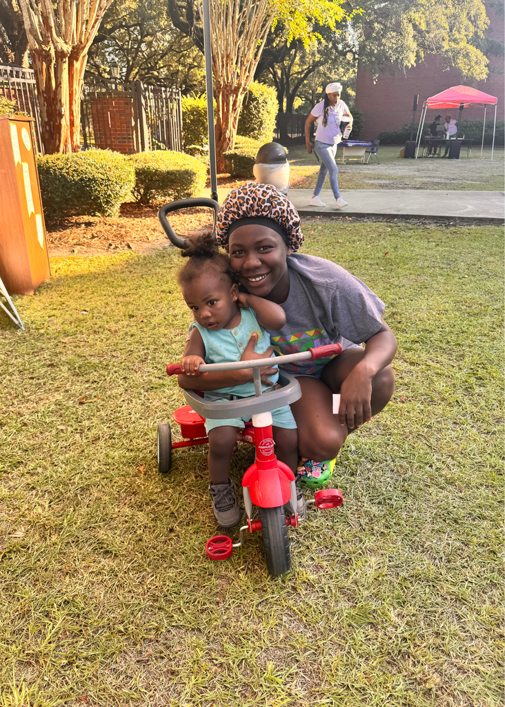 GCAE student and toddler on a red tricycle posing for a photo.