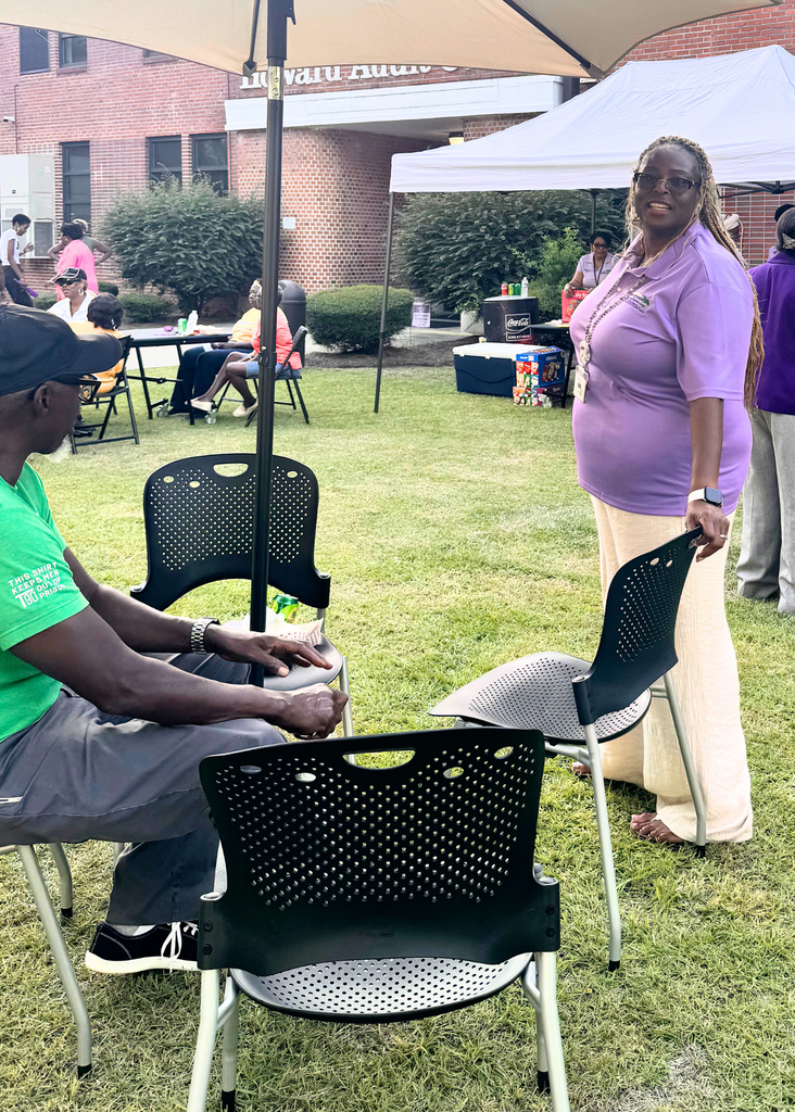 Tina Gilliard-Rice smiling for the camera with a community member seated under an umbrella wearing a green shirt.