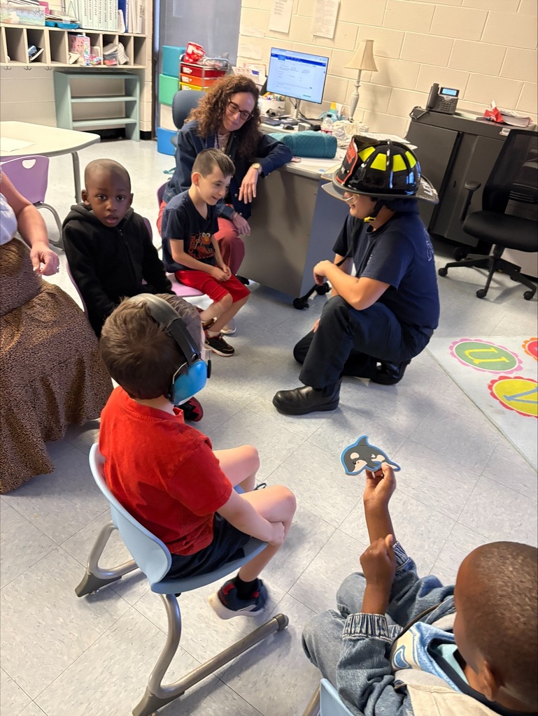 A Midway Fire Rescue firefighter kneels and talks with a small group of Waccamaw Elementary students during a classroom fire safety lesson.