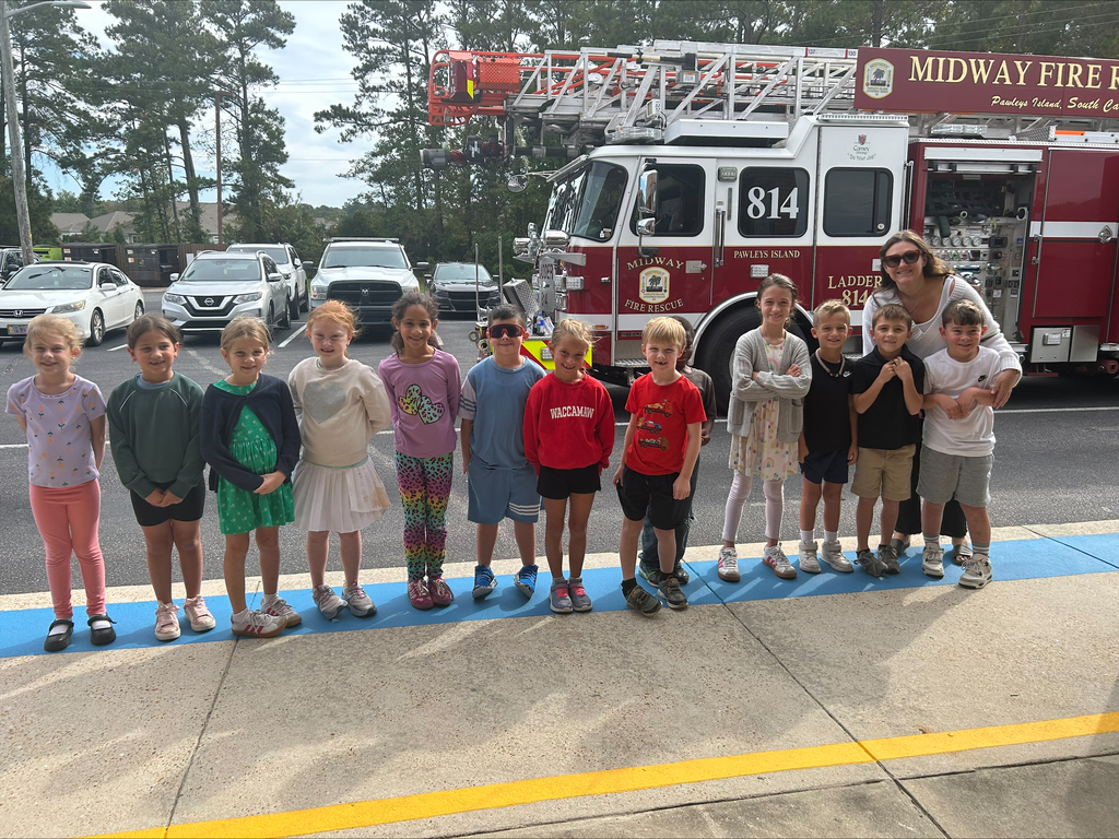 A group of Waccamaw Elementary students and their teacher smile together in front of a Midway Fire Rescue ladder truck during the school’s fire safety visit.