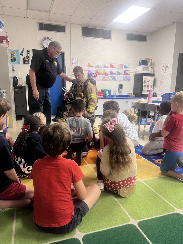 Waccamaw Elementary students gather on a classroom rug as a Midway Fire Rescue firefighter demonstrates firefighting gear and equipment during a fire safety lesson.
