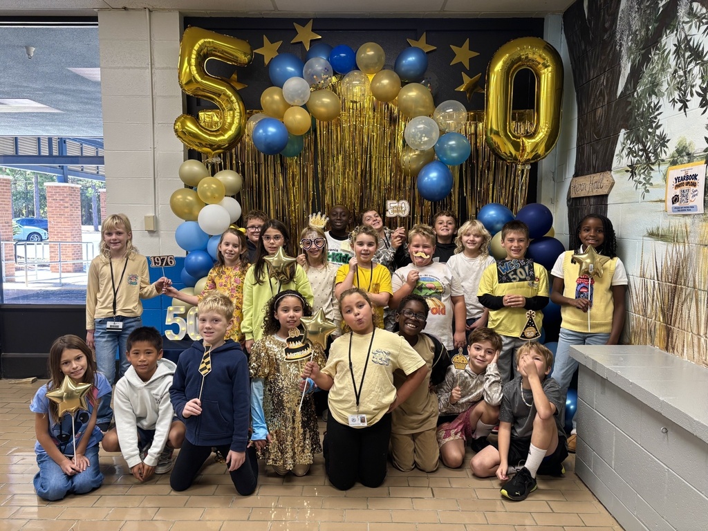 A large group of students poses together in front of the 50th celebration photo backdrop.