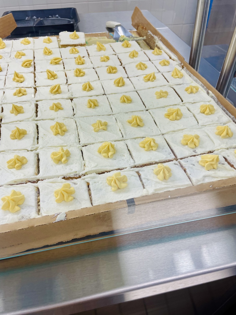 A tray of individual squares of white-frosted cake, each topped with a small swirl of yellow frosting.