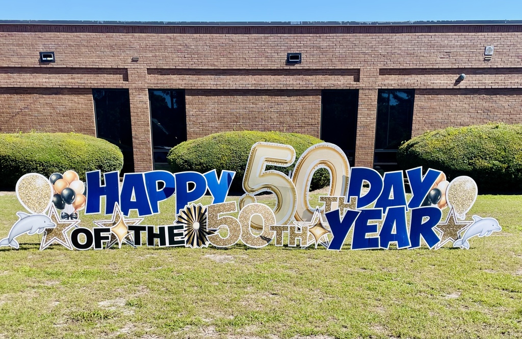 A large blue, gold, and white outdoor sign reads “Happy 50th Day of the 50th Year” in front of Waccamaw Elementary.