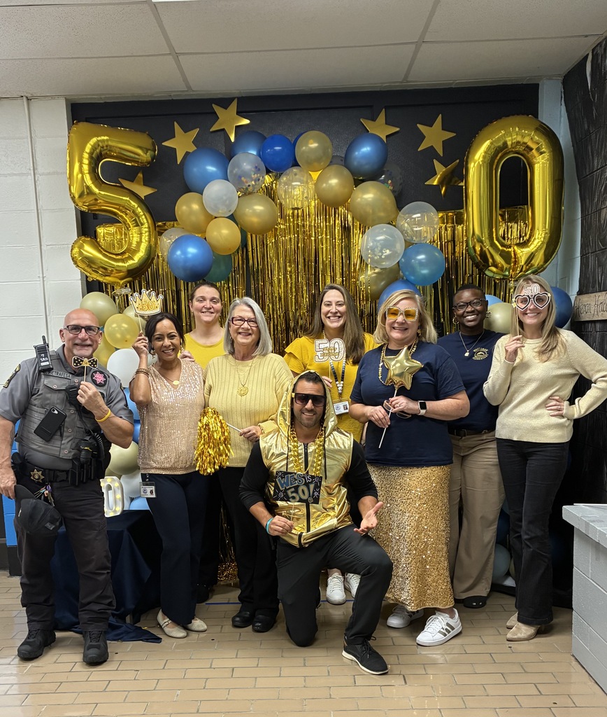 A  group of staff poses in front of the blue and gold balloon photo station.