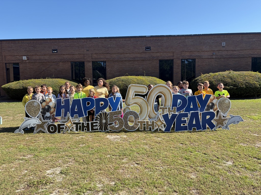 Students pose behind the large blue and gold 50th Day celebration sign outside the school.