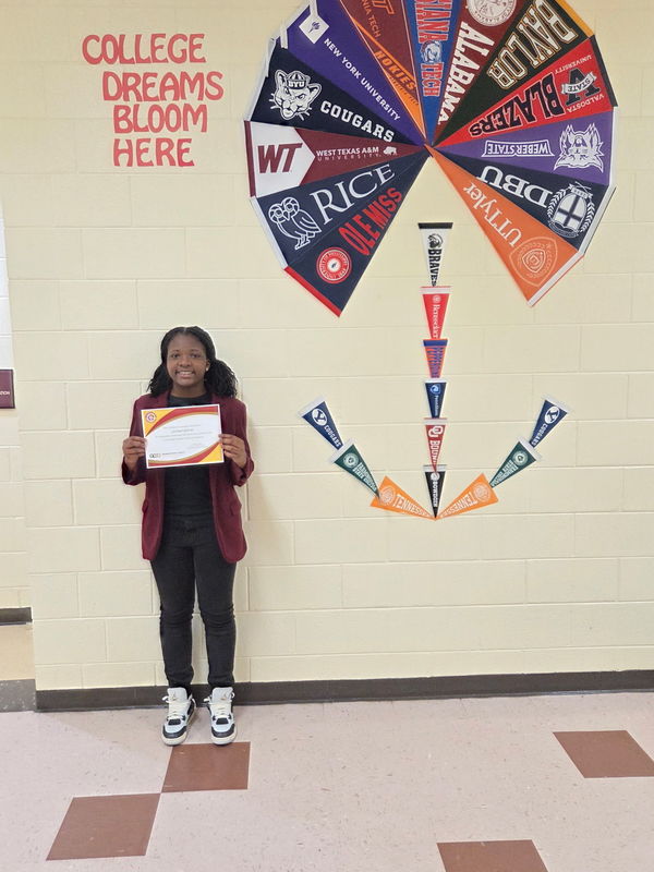 Female student standing by wall and holding a certificate.