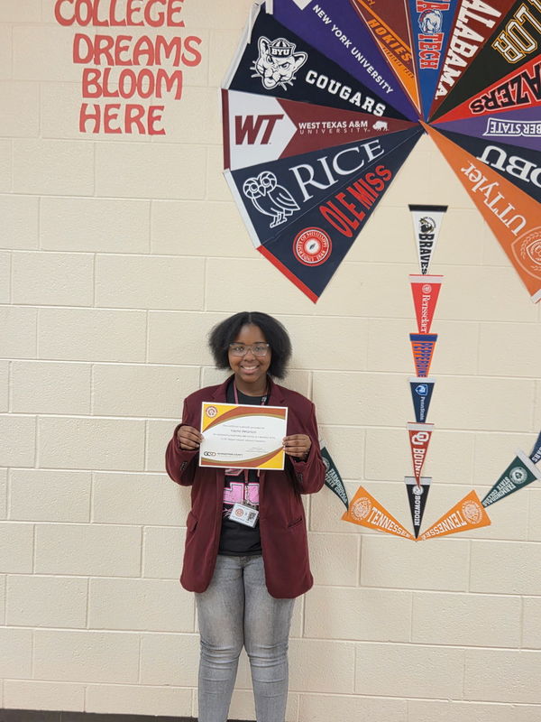 Female student standing by wall and holding certificate.