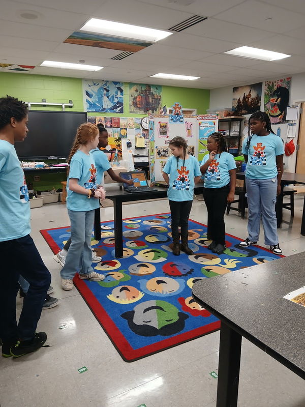 Students wearing blue t-shirts and standing on rug.