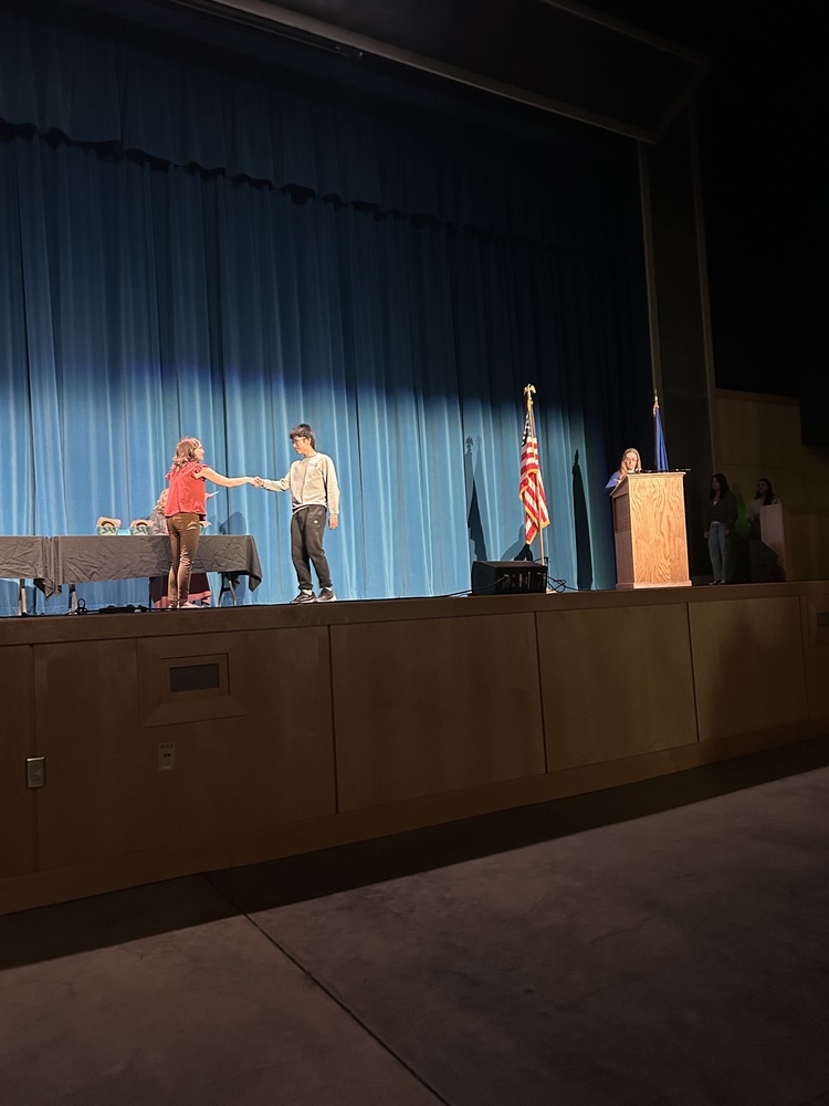 Spring 2026 Academic Awards Ceremony. A student crosses the stage to receive an award from school administrators after their name is announced by Student Services staff.