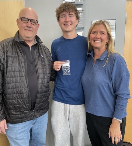 A student holds up his academic pin joined by his family following the ceremony.