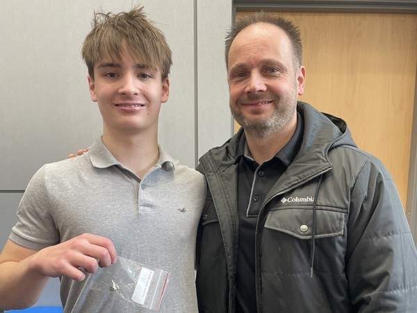 A student holds up his academic pin joined by family following the ceremony.
