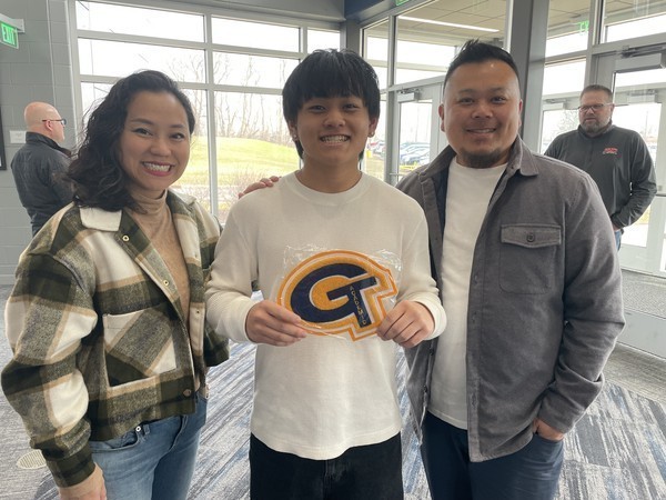 A student holds up his academic letter joined by family following the ceremony.