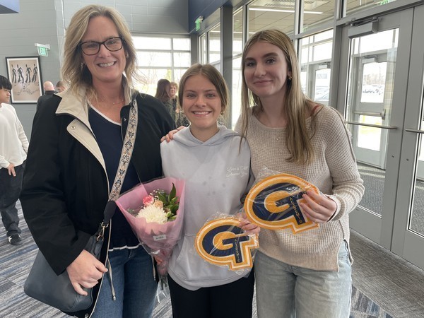 Two students hold up their academic letter joined by family, holding flowers, following the ceremony.