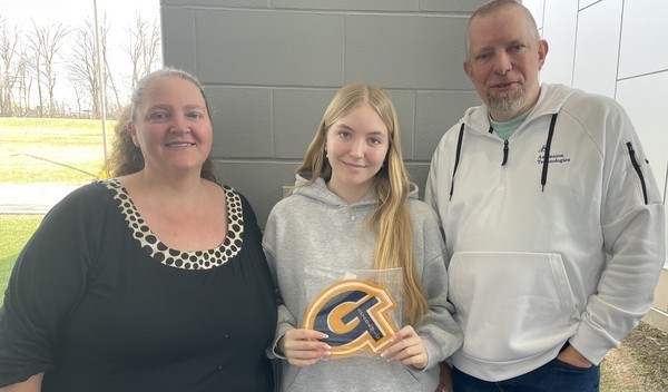 A student holds up her academic letter joined by her family following the ceremony.
