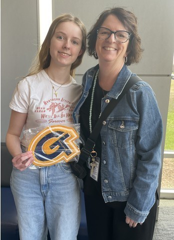 A student holds up her academic letter joined by family following the ceremony.