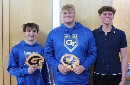 Three male students stand together with two holding up their academic letter for celebration after the ceremony.