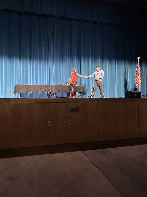 Spring 2026 Academic Awards Ceremony. A student crosses the stage to receive an award from school administrators after their name is announced by Student Services staff.
