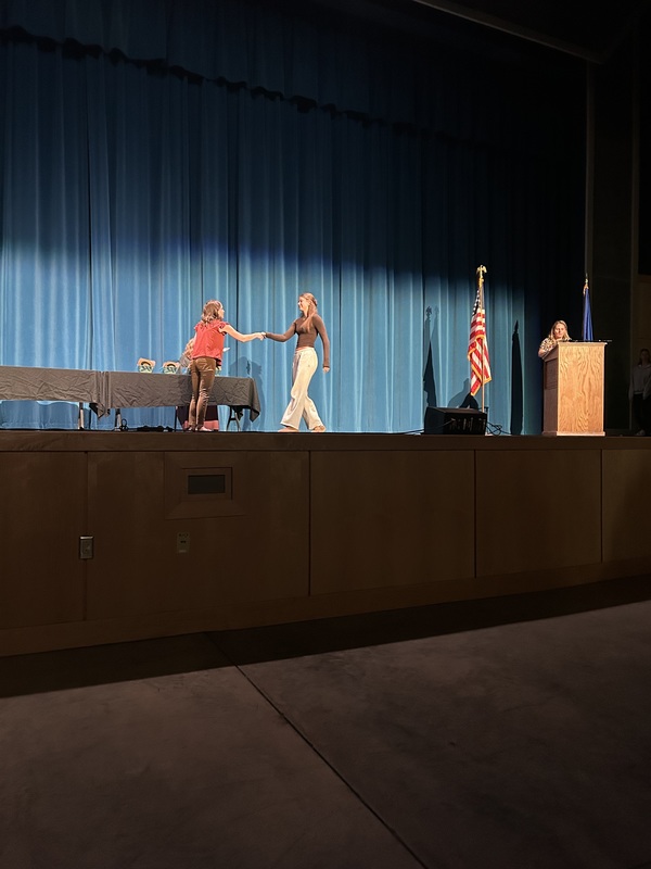 Spring 2026 Academic Awards Ceremony. A student crosses the stage to receive an award from school administrators after their name is announced by Student Services staff.