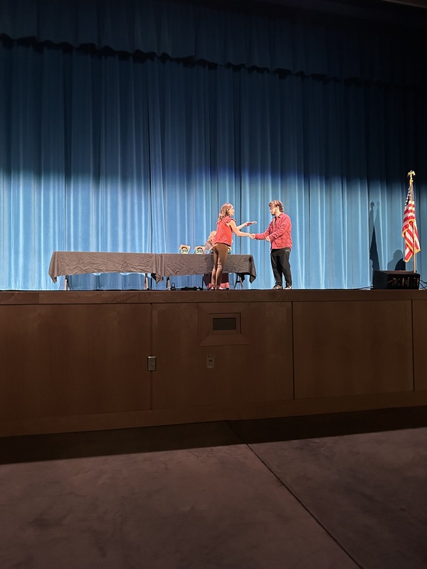 Spring 2026 Academic Awards Ceremony. A student crosses the stage to receive an award from school administrators after their name is announced by Student Services staff.