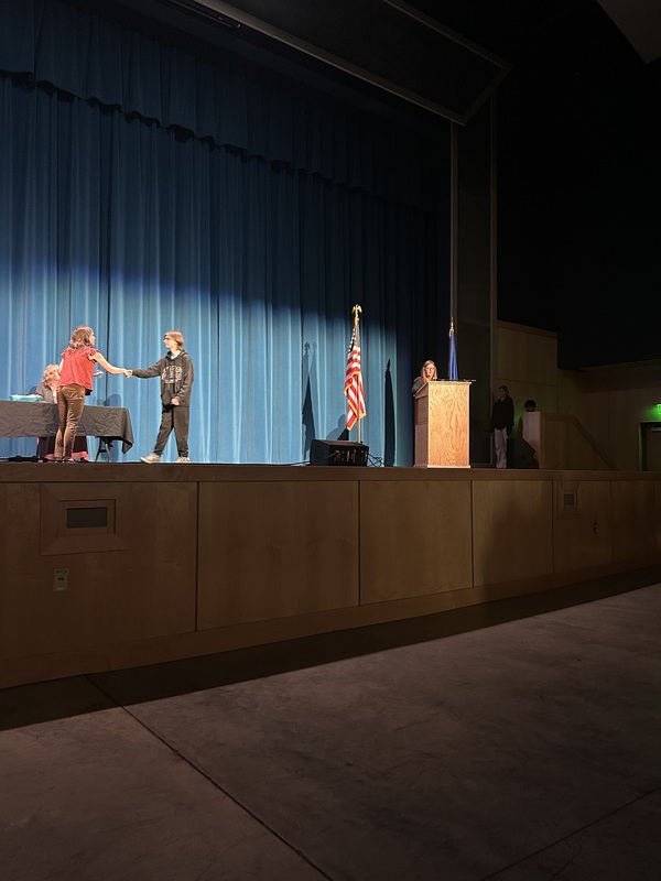 Spring 2026 Academic Awards Ceremony. A student crosses the stage to receive an award from school administrators after their name is announced by Student Services staff.