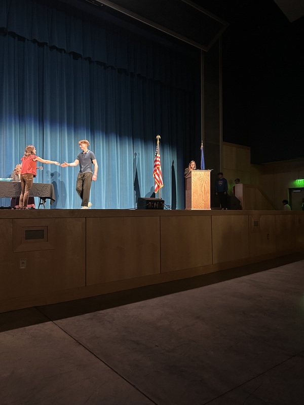 Spring 2026 Academic Awards Ceremony. A student crosses the stage to receive an award from school administrators after their name is announced by Student Services staff.