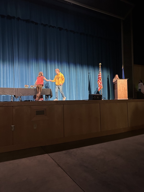 Spring 2026 Academic Awards Ceremony. A student crosses the stage to receive an award from school administrators after their name is announced by Student Services staff.