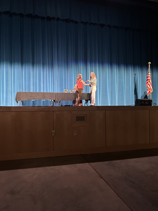 Spring 2026 Academic Awards Ceremony. A student crosses the stage to receive an award from school administrators after their name is announced by Student Services staff.