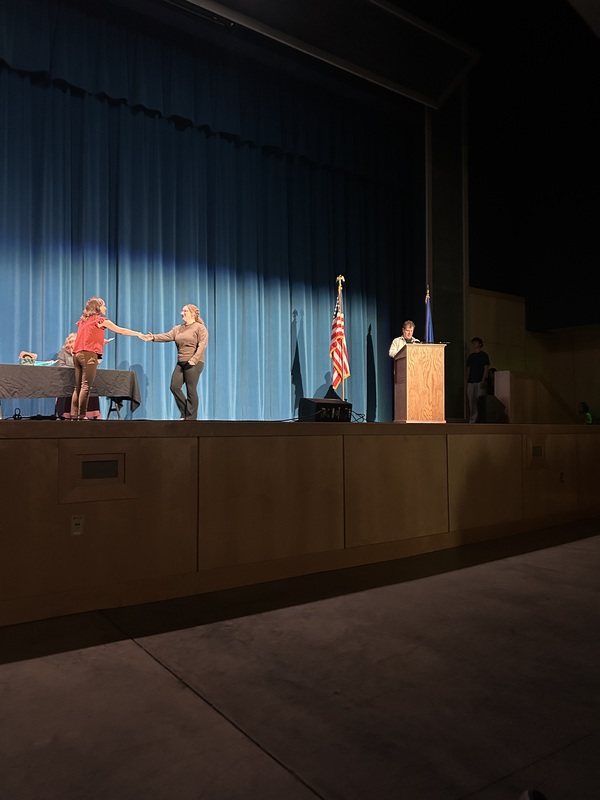 Spring 2026 Academic Awards Ceremony. A student crosses the stage to receive an award from school administrators after their name is announced by Student Services staff.