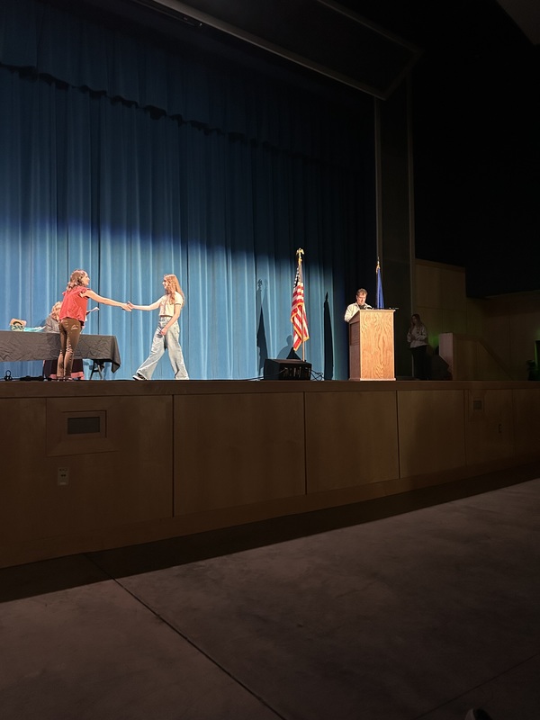 Spring 2026 Academic Awards Ceremony. A student crosses the stage to receive an award from school administrators after their name is announced by Student Services staff.