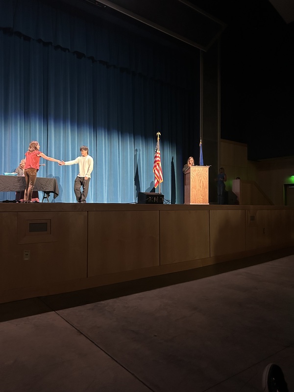 Spring 2026 Academic Awards Ceremony. A student crosses the stage to receive an award from school administrators after their name is announced by Student Services staff.