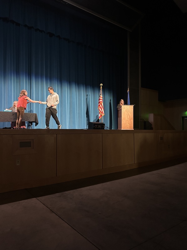 Spring 2026 Academic Awards Ceremony. A student crosses the stage to receive an award from school administrators after their name is announced by Student Services staff.