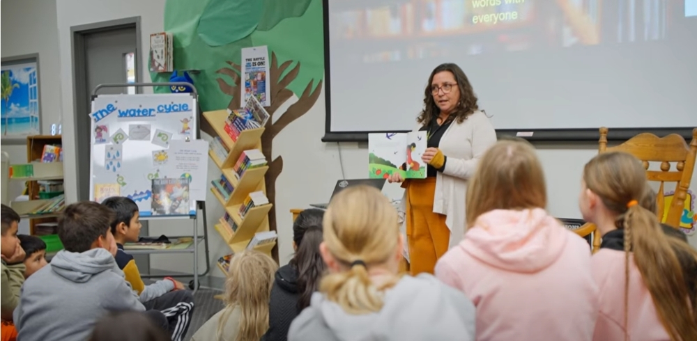 teacher holding up a picture book in front of elementary students