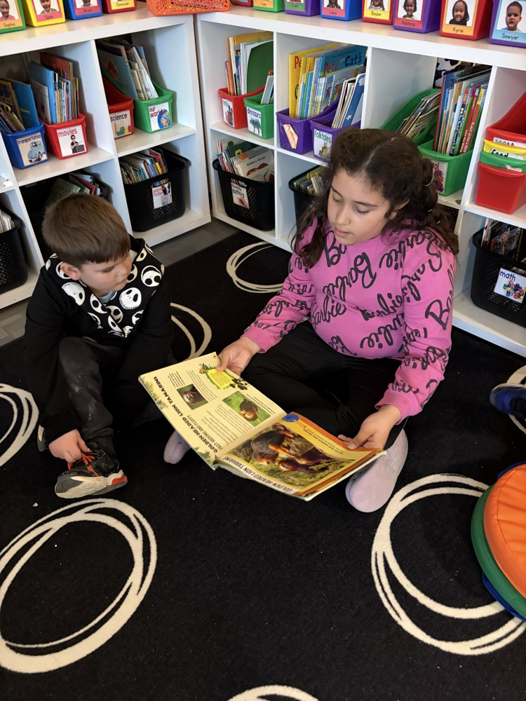 two students reading a book together on a carpet