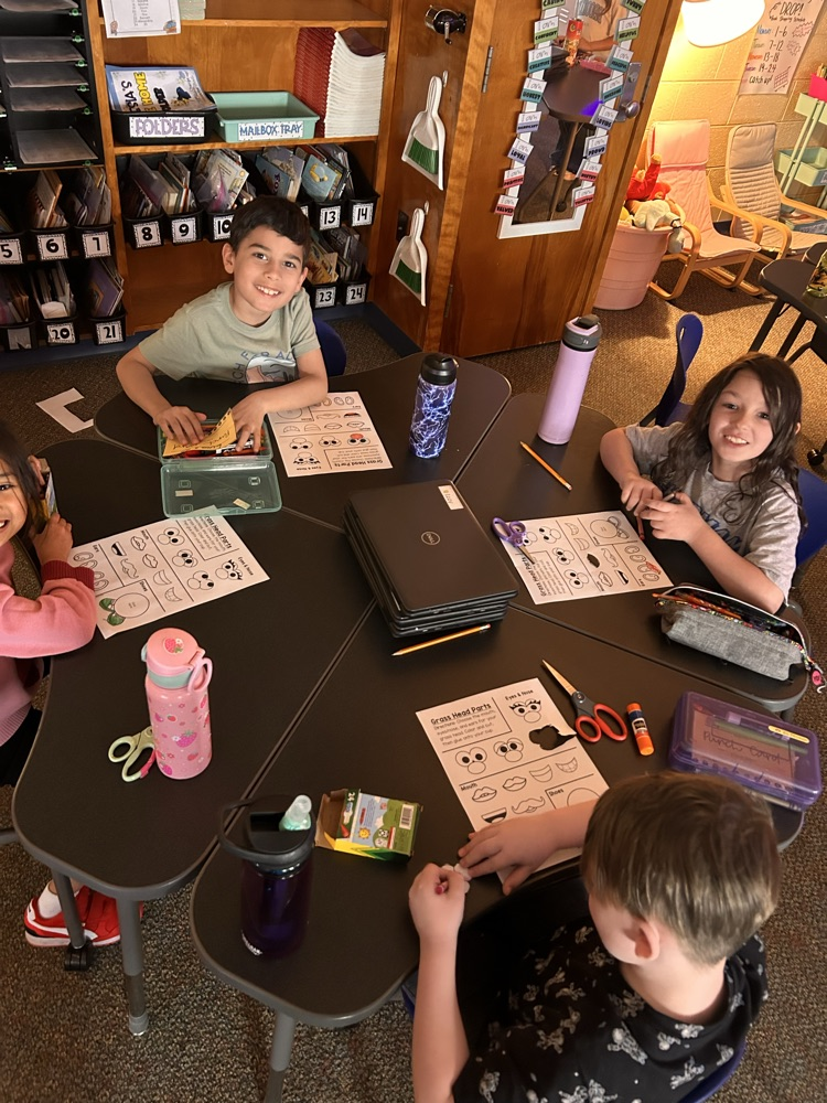 Elementary students sitting at desks creating and getting ready to plant grass as they begin their new unit on living things.