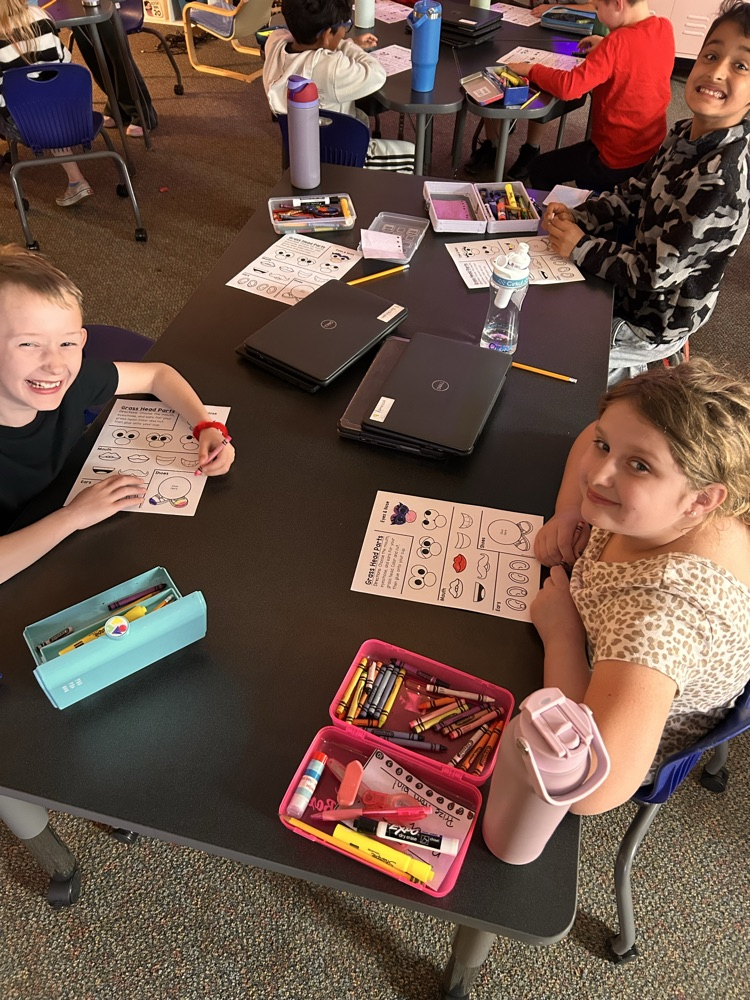 Elementary students sitting at desks creating and getting ready to plant grass as they begin their new unit on living things.