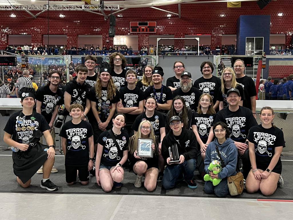 Group photo of students and coaches with plaques and awards