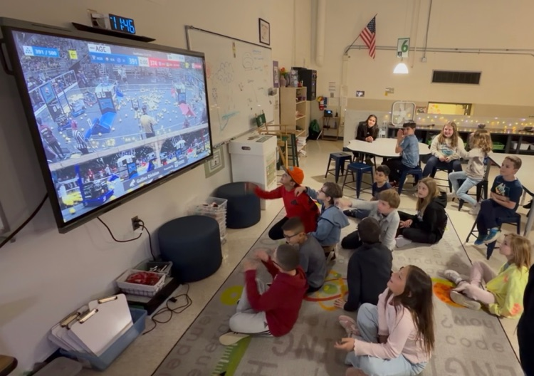 STEM students sitting on the carpet in STEM Tech watching on the Promethean Board Carlson Terror Bytes competing at Robotics Worlds
