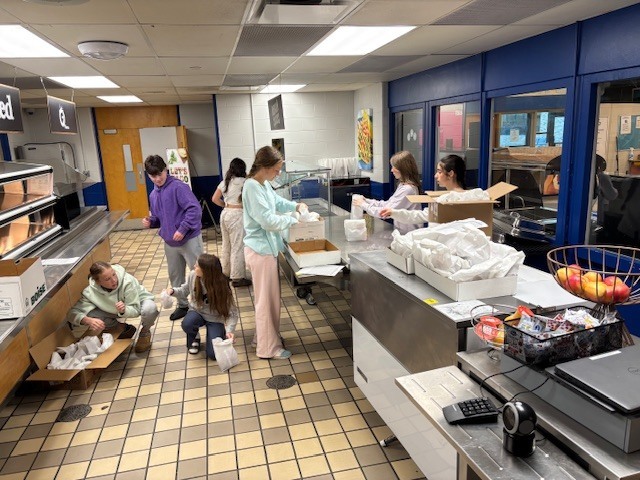 Students are in the cafeteria organizing breakfasts into boxes for distribution 