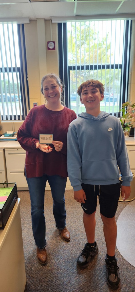 A student stands with a secretary while the secretary holds up a sign