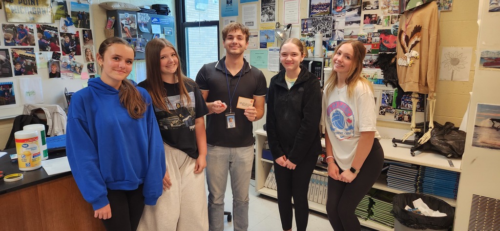 4 students stand with a teacher and the teacher is holding up a note