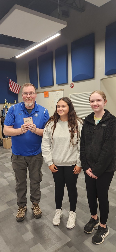 A teacher is standing next to two students and smiling