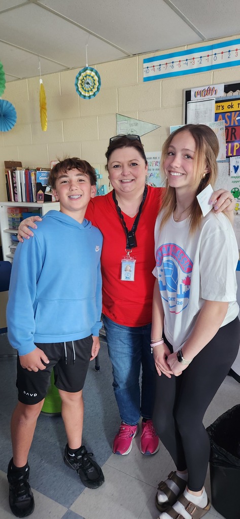 A student stands to the left of a teacher and a student stands to the right of a teacher and the teacher has her hands around the students' shoulders