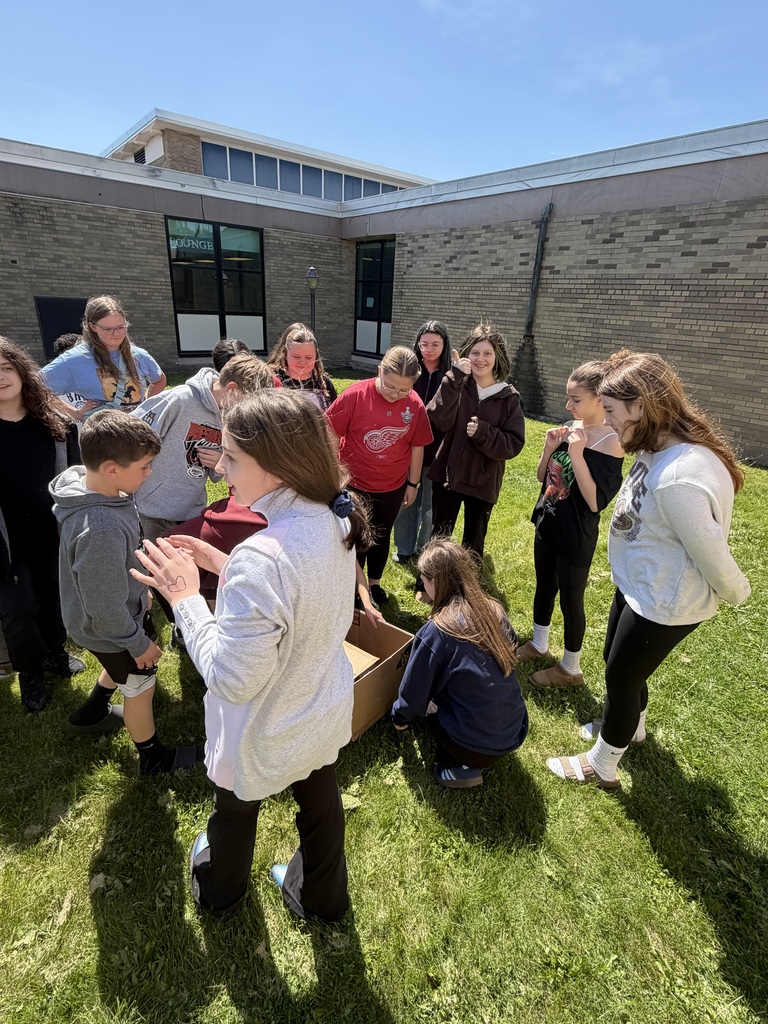 Students are looking on as they prepare to gather up the baby ducks and release them to their mother.  Students are in a huddle around the box.  