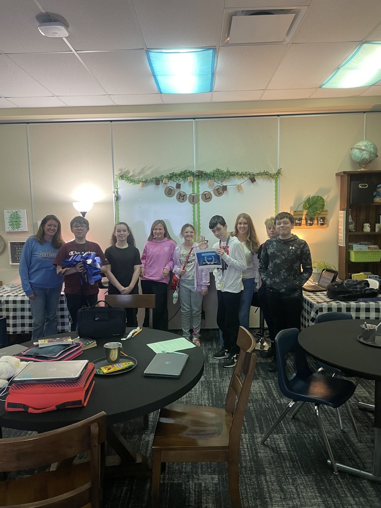 Mrs. Hobbins and Mrs. Gillum's Advisory class standing under a smile sign and smiling for the camera holding a sign and bow